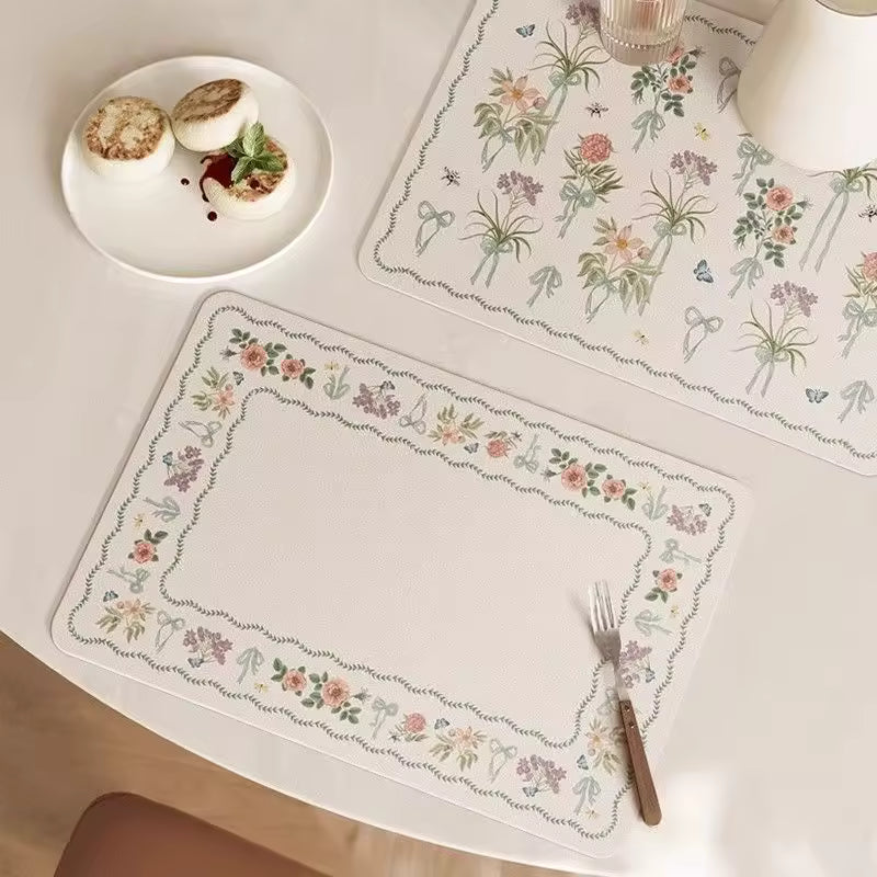 Two rectangular table mats with delicate floral borders in soft pastel colors and all over designed botanical floral mat.