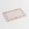 A rectangular placemat with rounded corners, featuring a delicate floral border in soft pastel shades of pink, purple, green, and blue, set against a clean beige background.